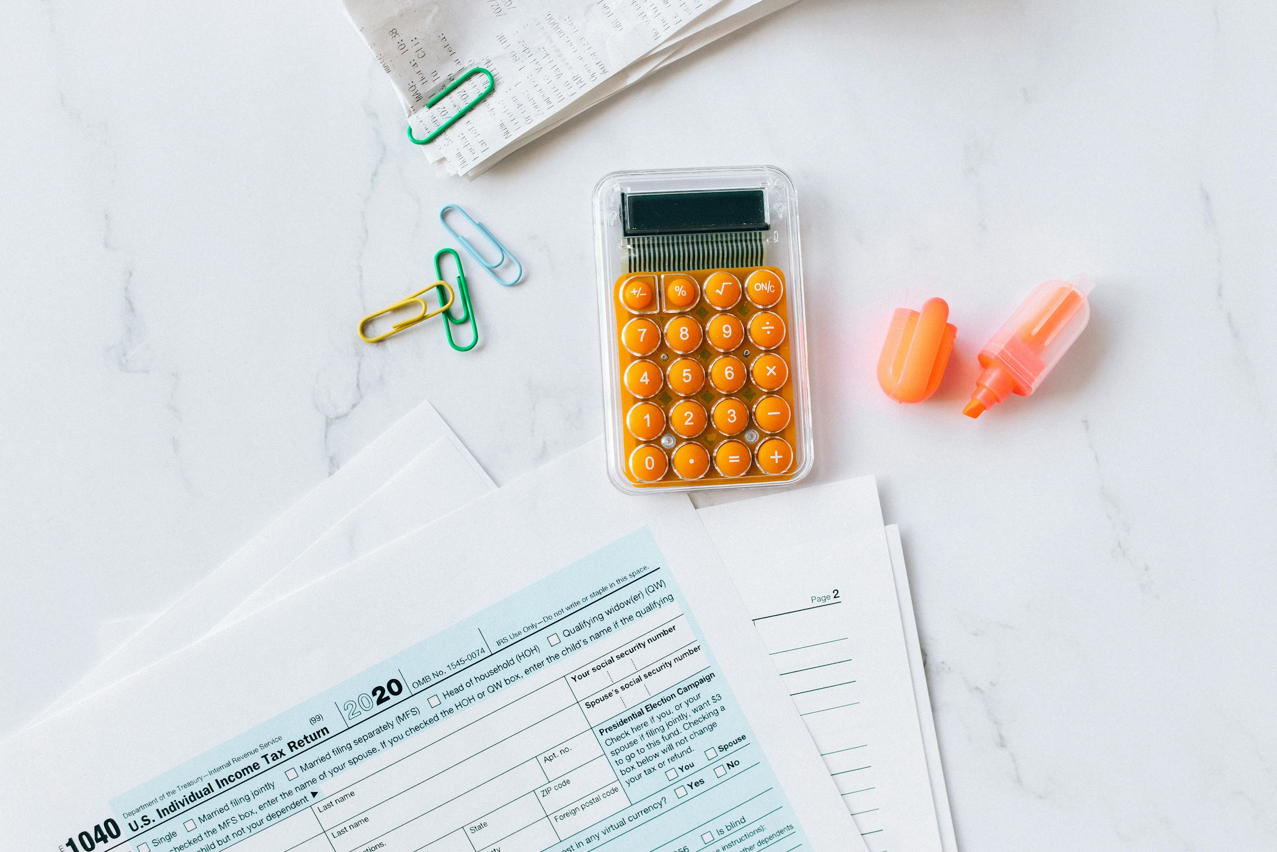 A flat lay image of tax forms, calculator, and office supplies on a desk.